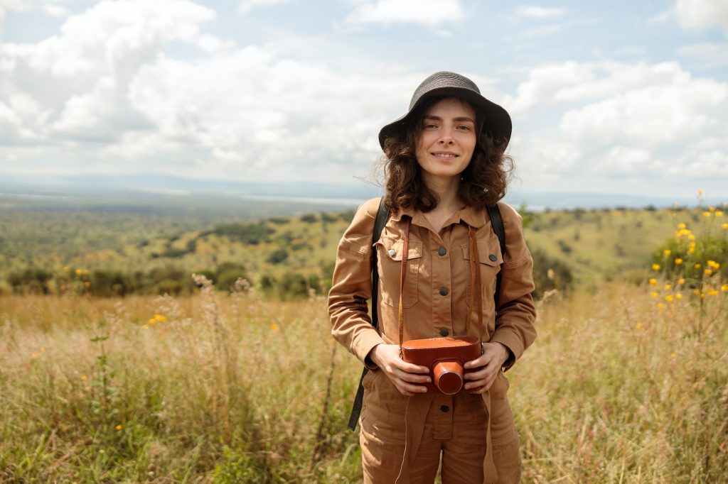Smiling female traveler posing and holding photo camera on safari